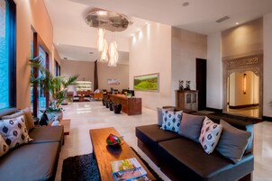 Um saguão moderno de hotel com balcão de recepção, área de estar com sofás e poltronas, e uma pintura grande na parede.