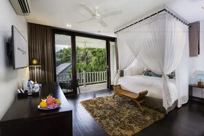 A bedroom with a bed, a desk, a chair, a bedside table, and a view of greenery outside. - Montigo Resorts Seminyak (Keroboken Kelod)