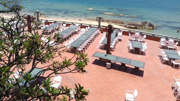 Terraço com mesas e cadeiras com vista para o mar, piso de azulejos e visual da praia e oceano.