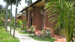 Edifício de tijolos com galeria coberta, rodeado por vegetação exuberante e palmeiras.