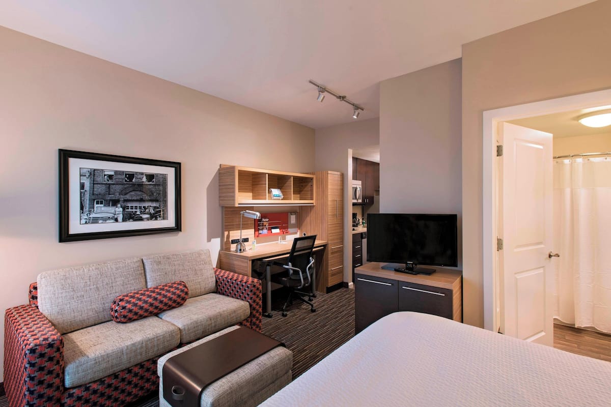 A hotel room with a bed, a sofa, a desk, a television, and a framed picture on the wall.