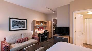 A hotel room with a bed, a sofa, a desk, a television, and a framed picture on the wall.