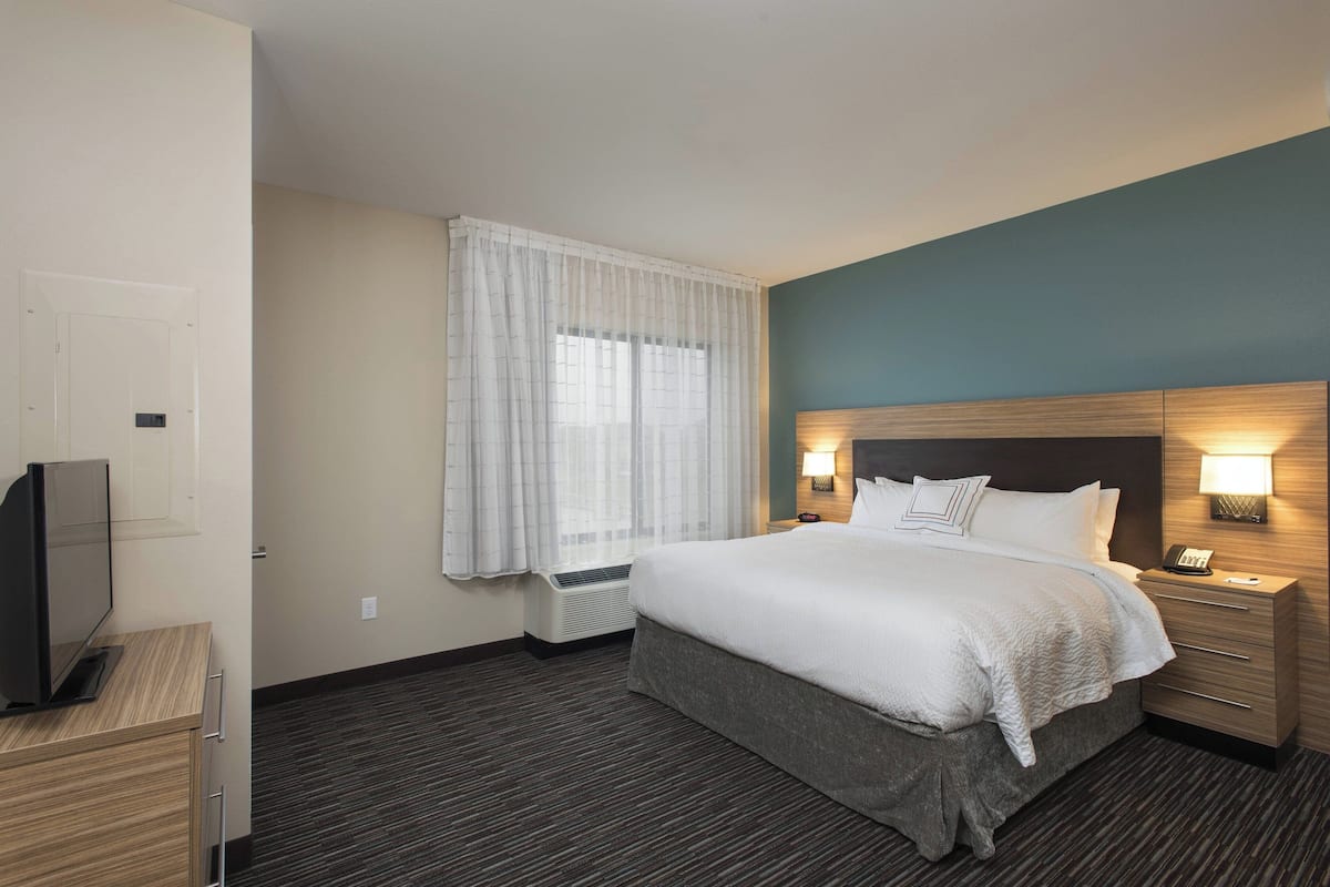 A hotel room with a bed, bedside tables, a TV, and a window with curtains.