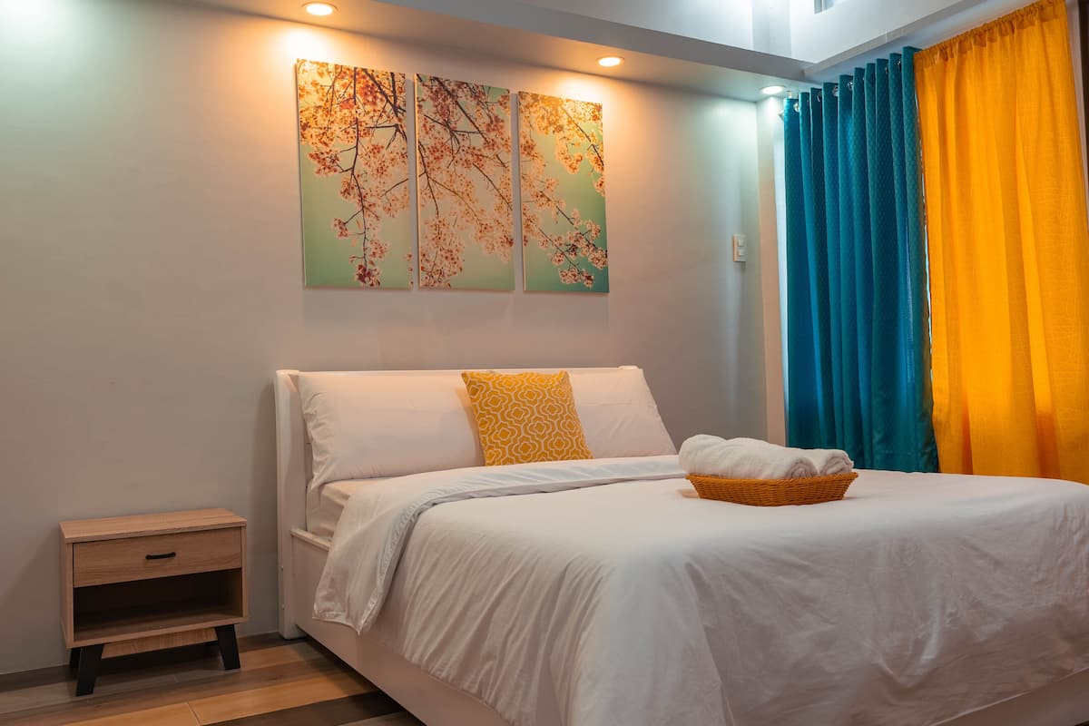 Una cama bien hecha con ropa blanca, una mesita de noche de madera y un cuadro colgado en la pared.
