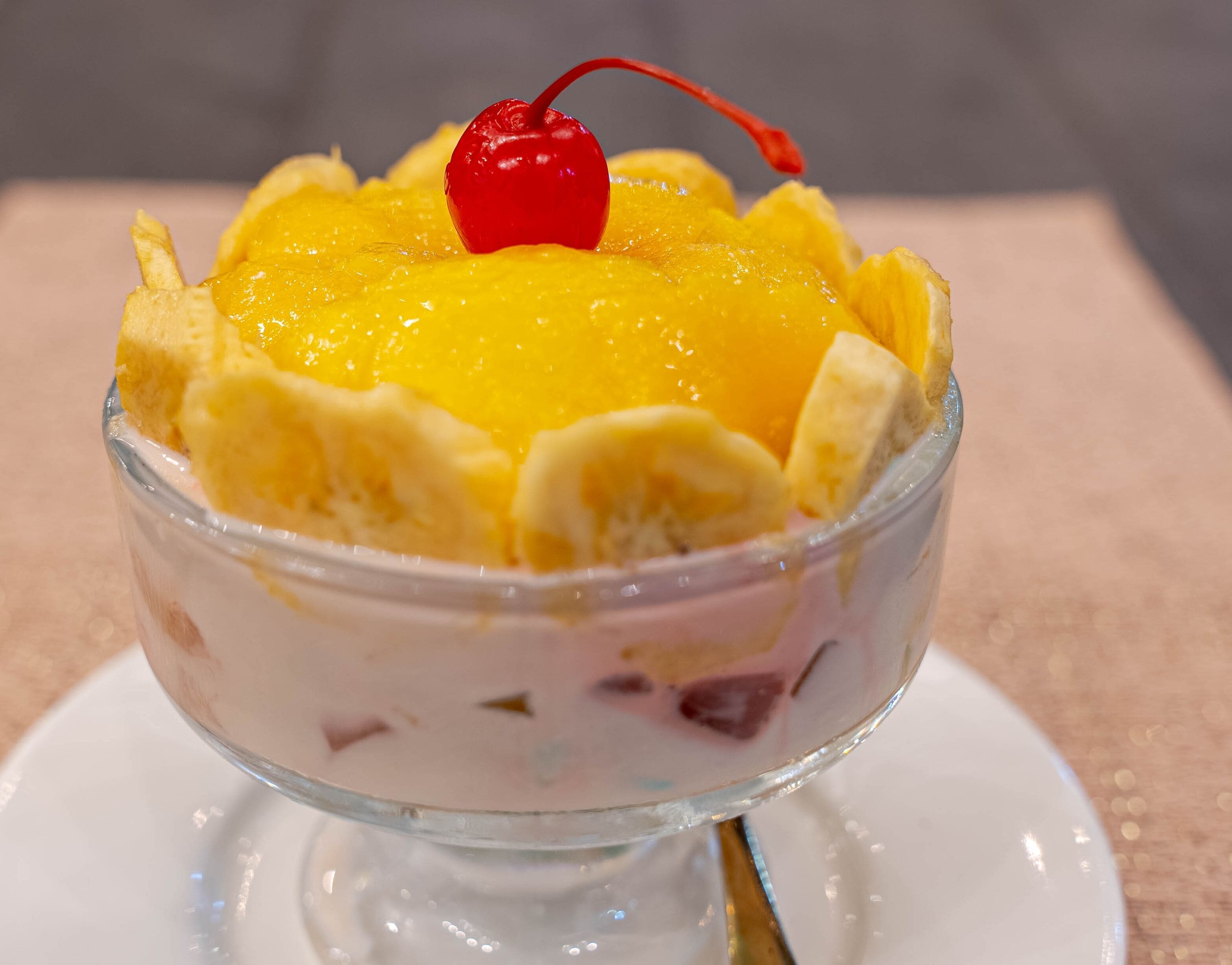 A dessert in a clear glass bowl with a cherry on top.