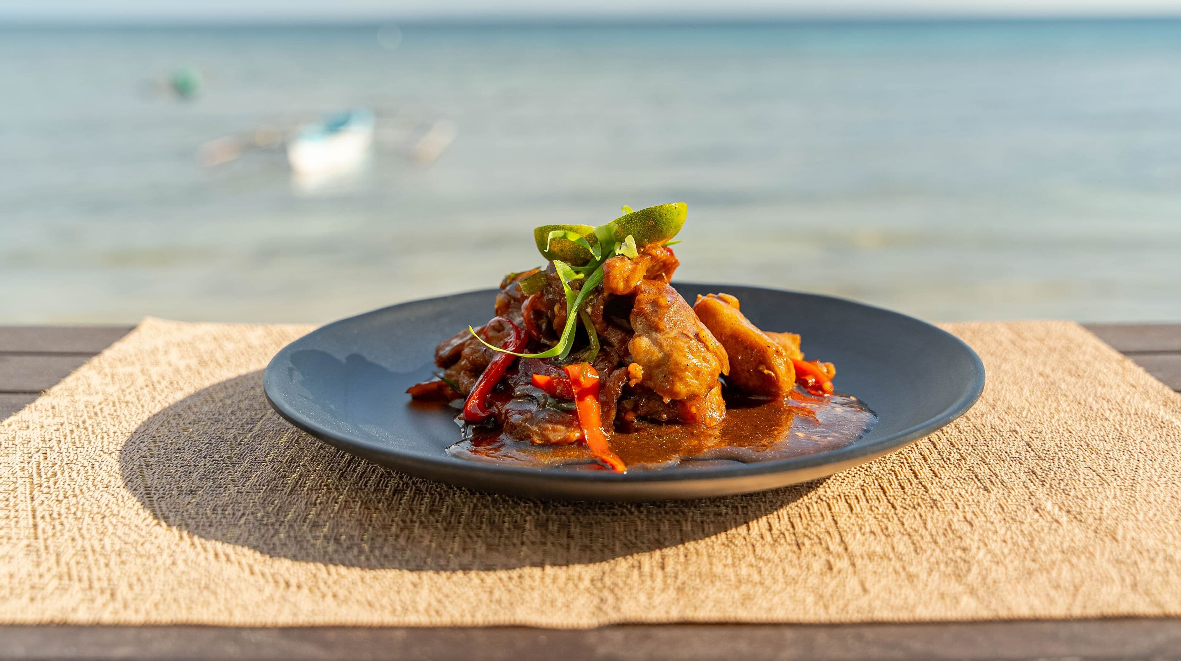 A plate of food on a textured mat with a body of water and a boat in the background.