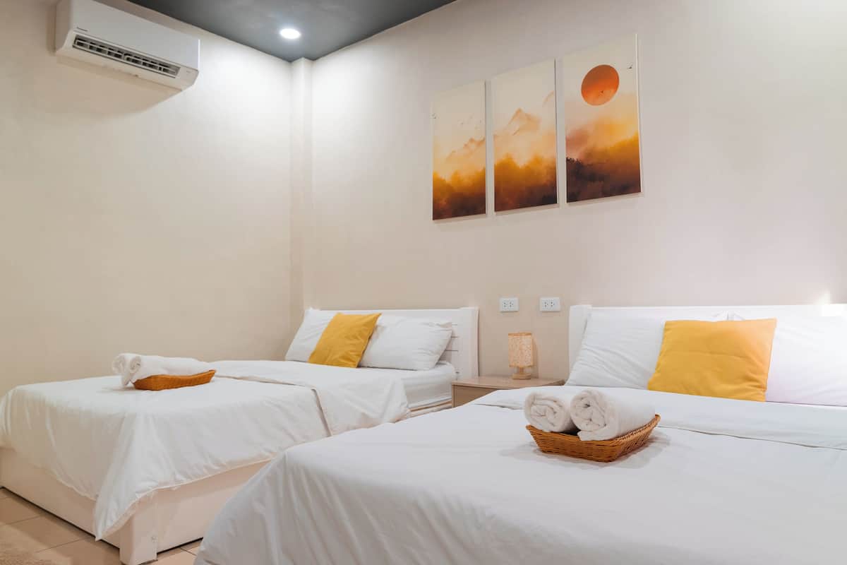Habitación de hotel con dos camas, ropa de cama blanca y aire acondicionado de pared.