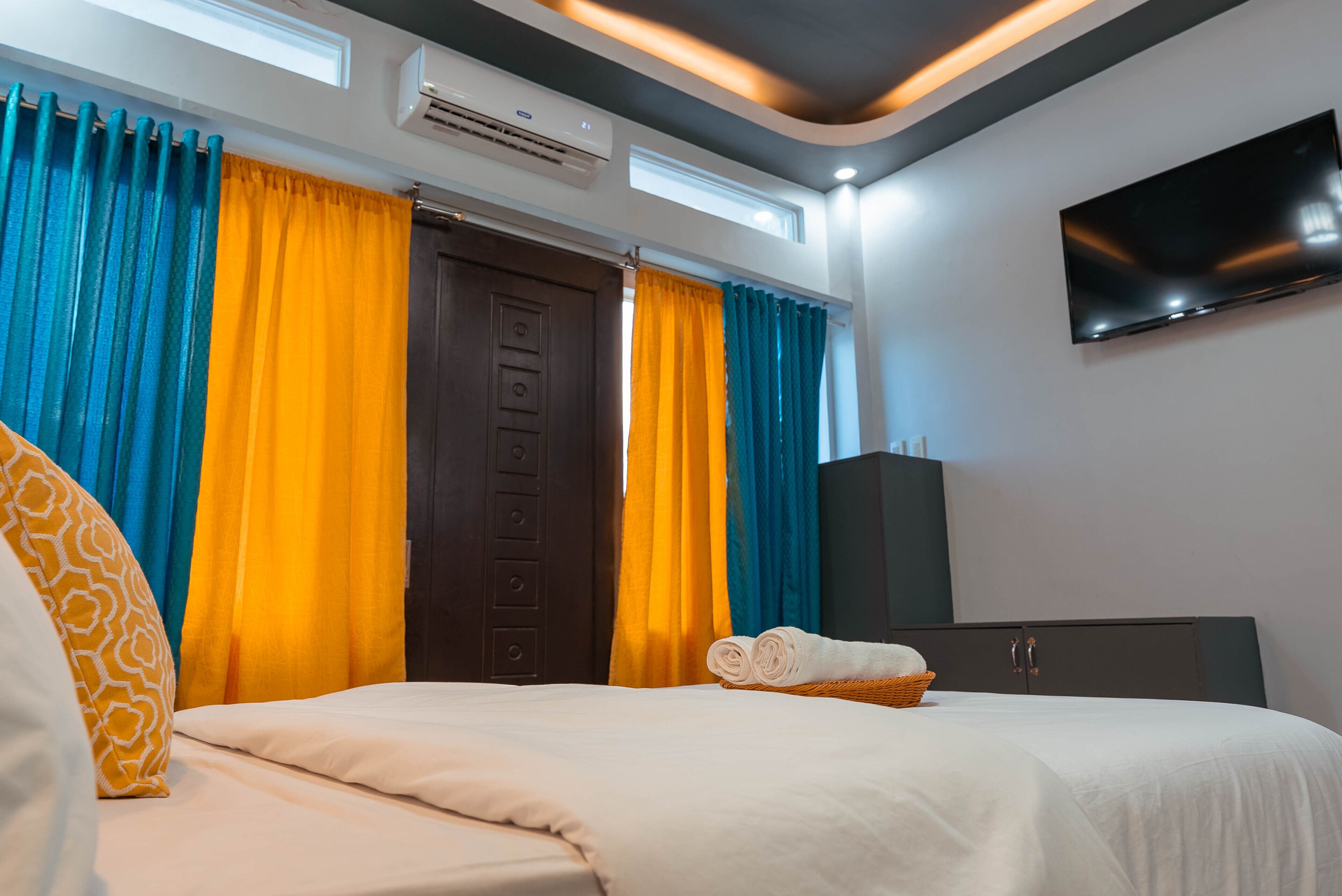 A hotel room with a bed, curtains, a TV, and an air conditioning unit.