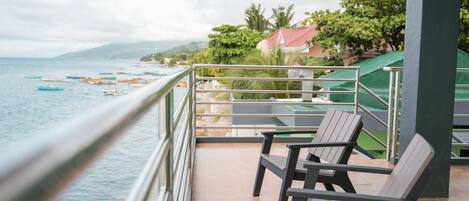 A balcony with a view of the sea and boats, two wooden chairs, and a green umbrella.