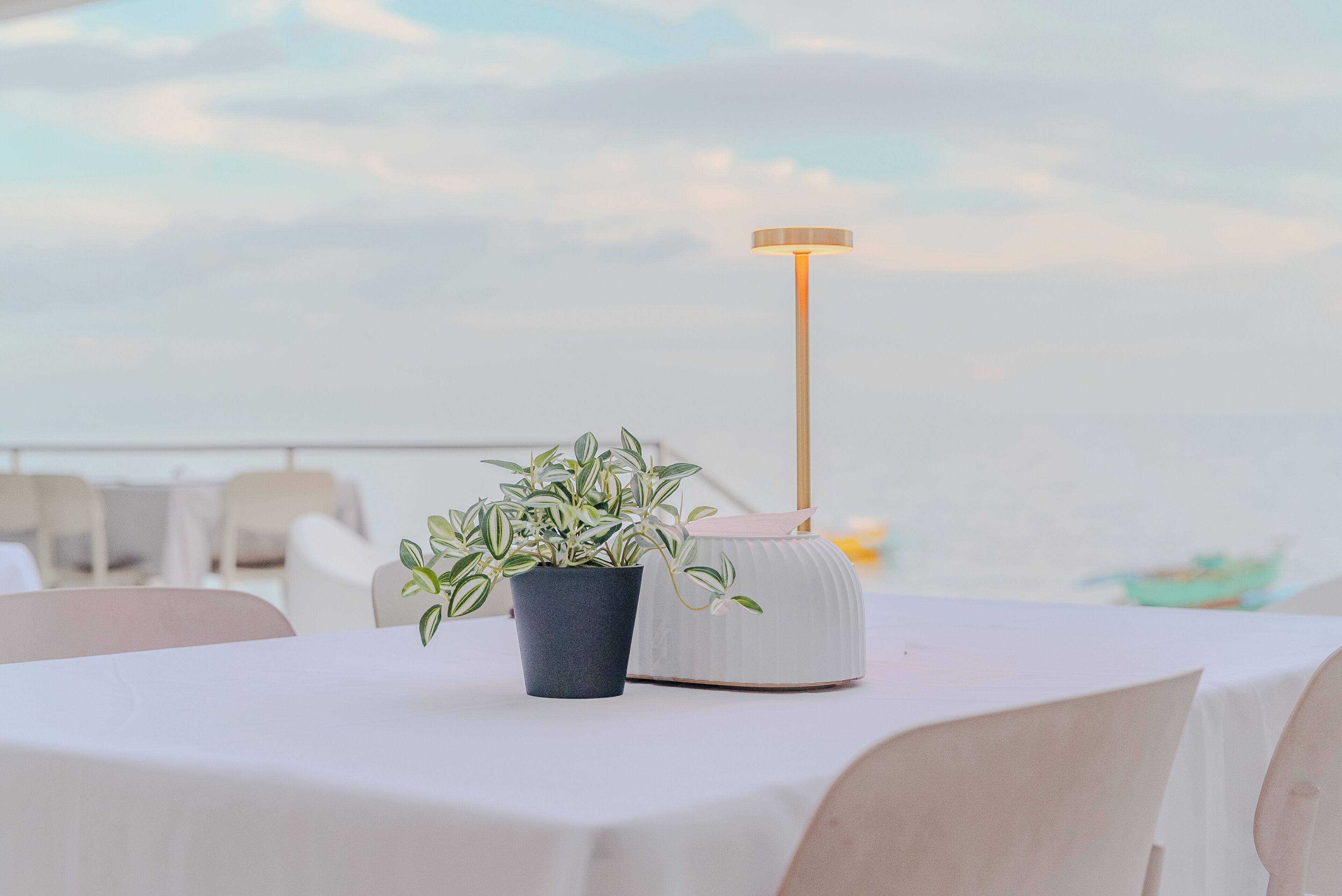 Una mesa con una planta en maceta y una lámpara blanca sobre un mantel.