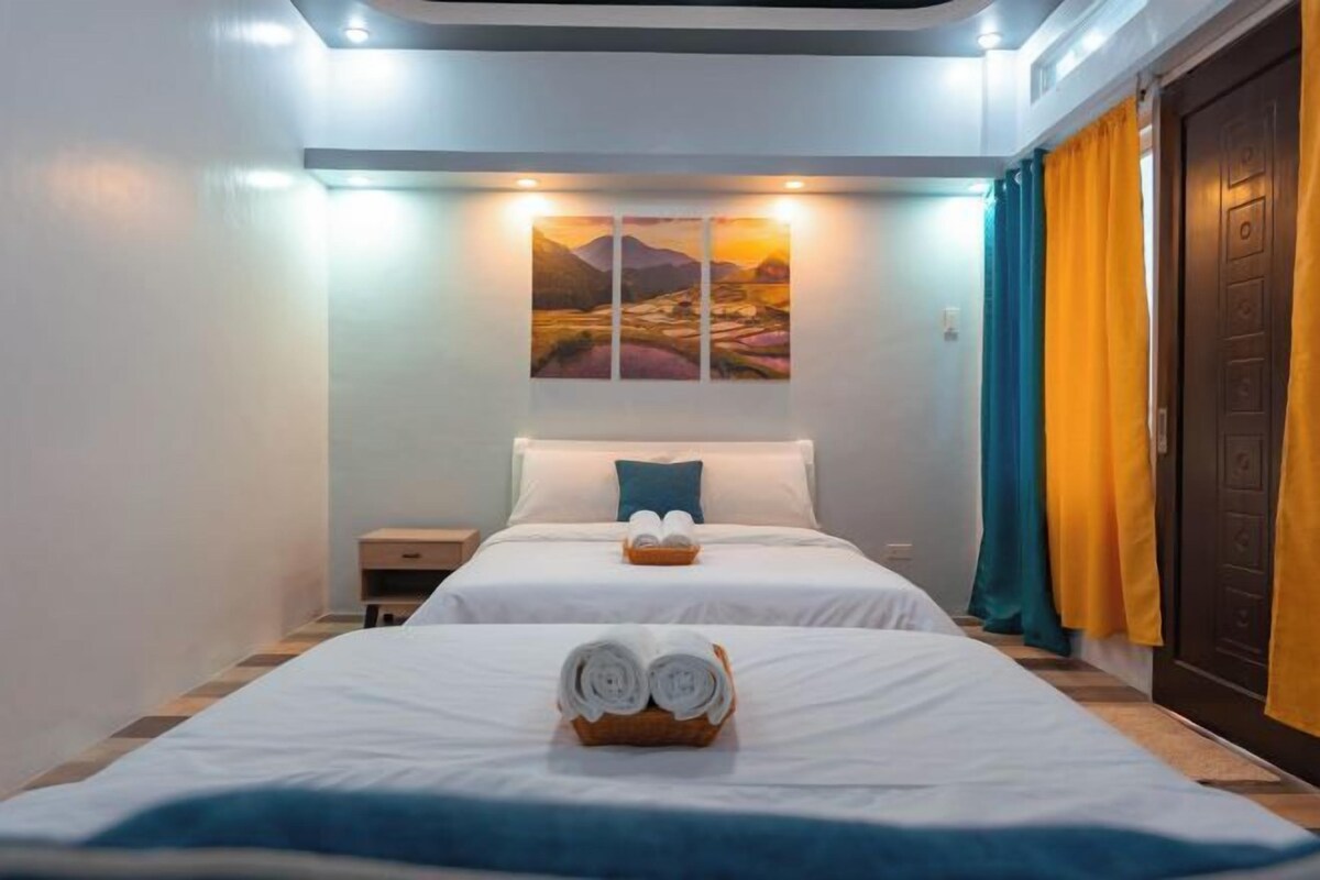 A hotel room with two beds, a painting on the wall, and a door with curtains.