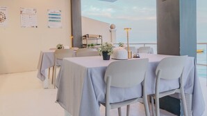 Un coin repas avec des tables disposées pour accueillir quatre personnes, une plante en pot et une vue sur la mer.