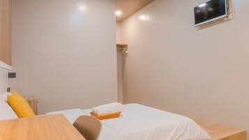 A bedroom with a bed, a wooden nightstand, a TV mounted on the wall, and a small shelf.