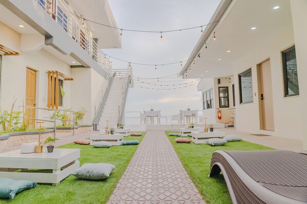 A modern hotel atrium with a central pathway, outdoor seating, and a staircase leading to an upper level.
