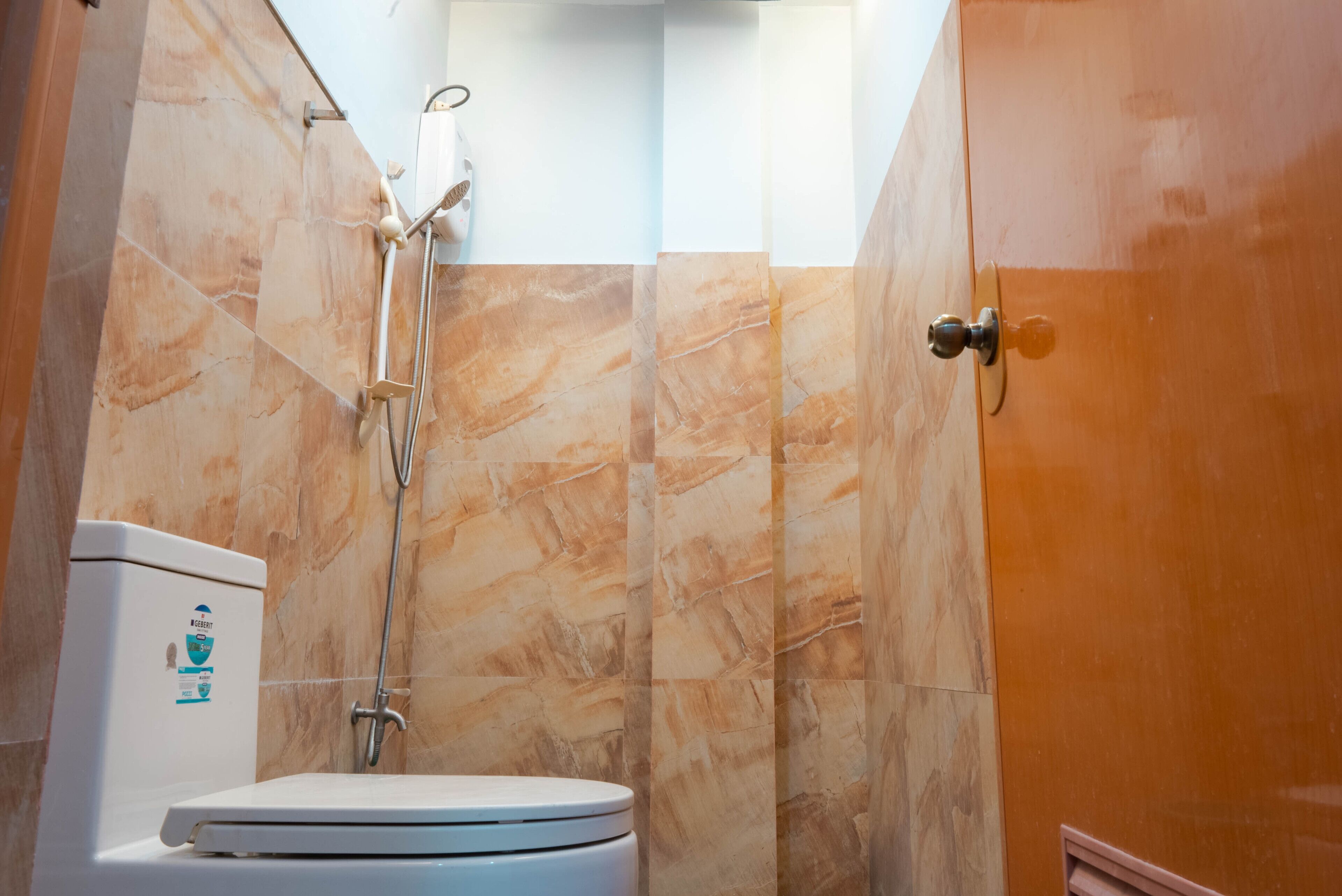 A bathroom with a toilet, shower, and a marble wall.