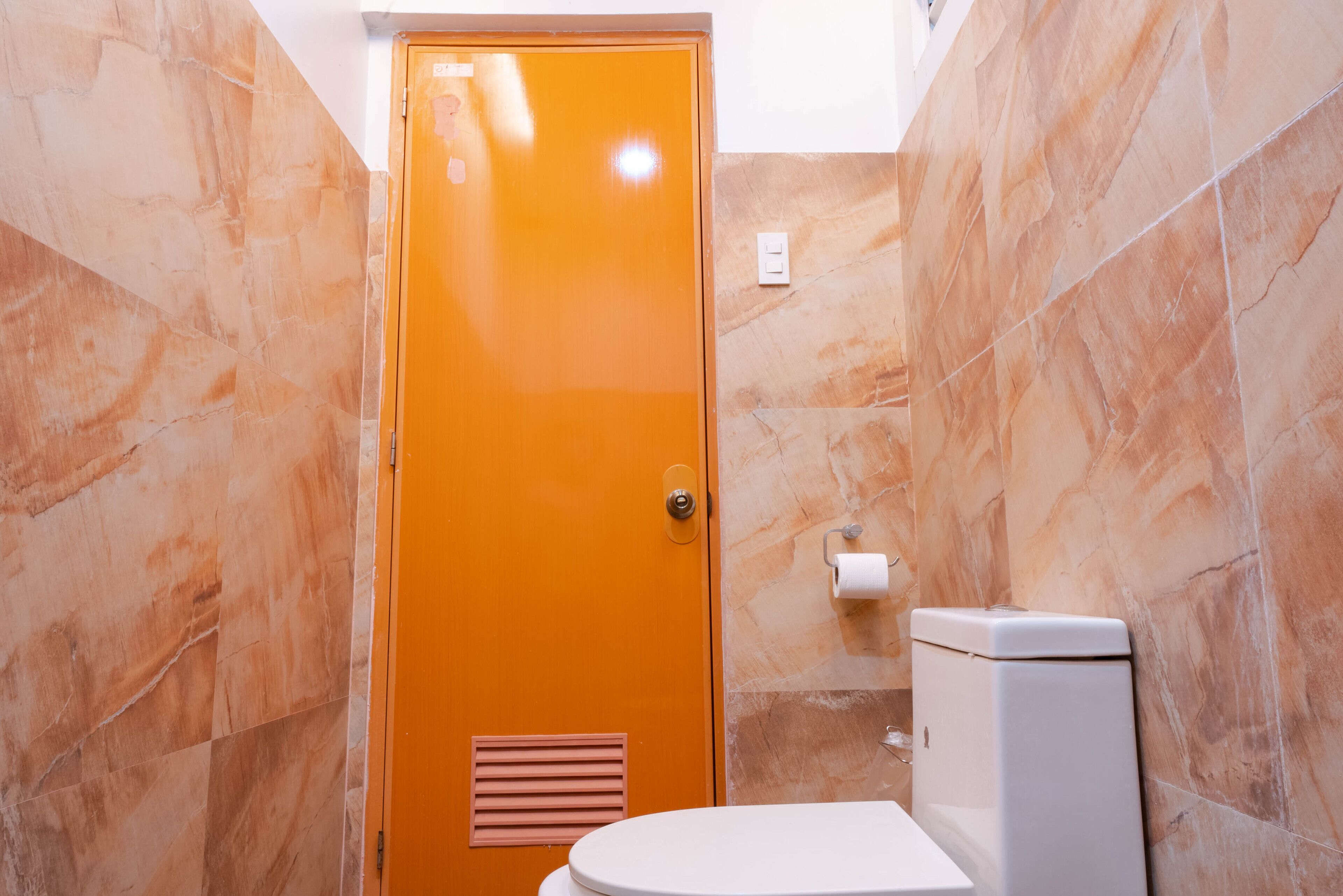 Et badeværelse med toilet, ventilationsrist og en marmorvæg.