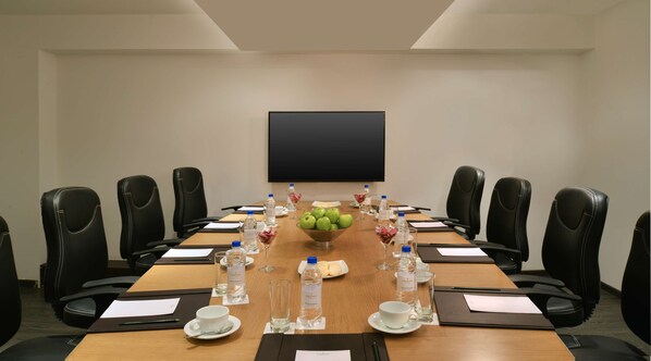 A conference room with a long table, black leather chairs, a large screen, and a bowl of green apples.