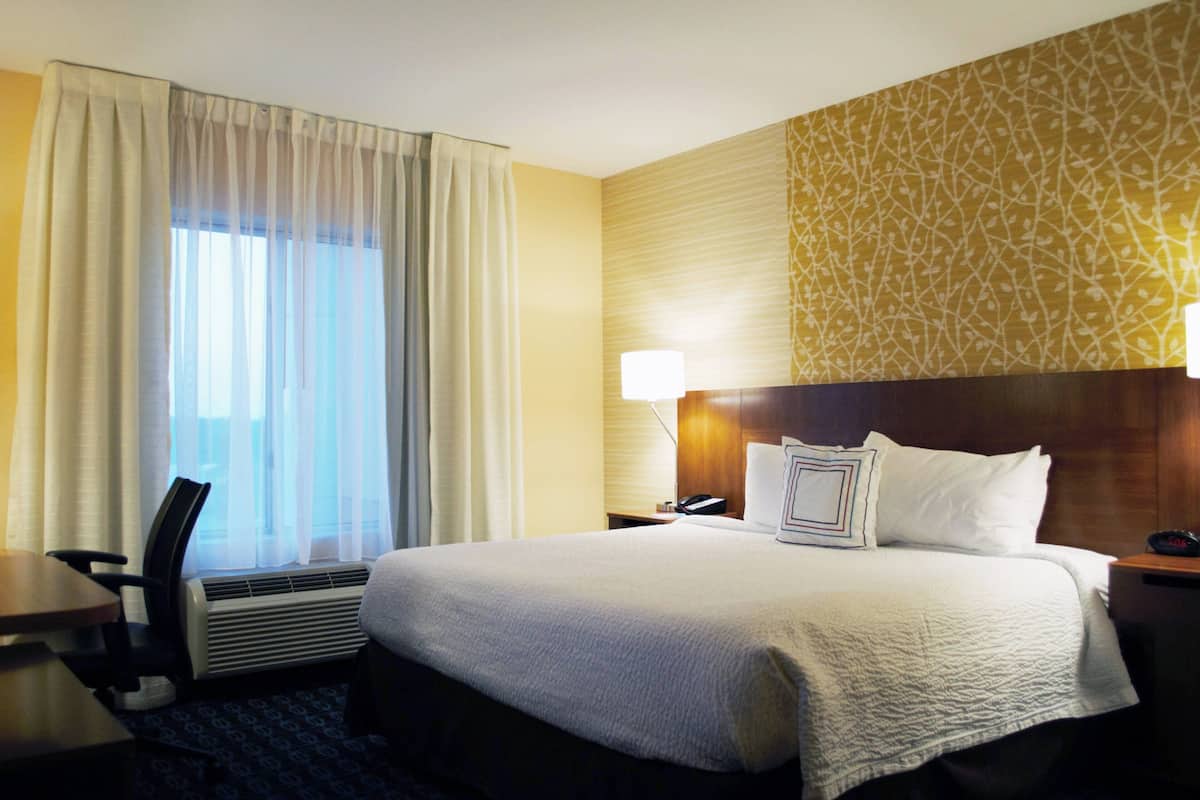 Ett hotellrum med en stor säng, ett skrivbord, en stol och ett fönster med gardiner.