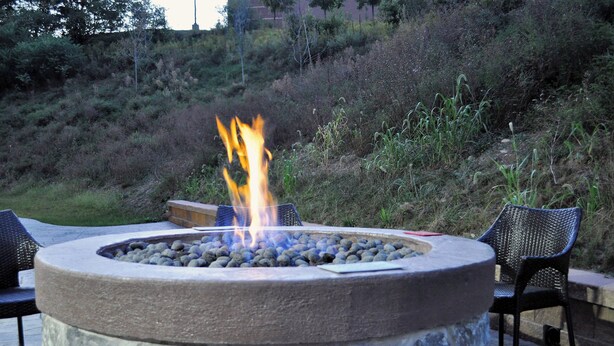 A stone fire pit with a fire burning, surrounded by chairs. - Fairfield Inn & Suites Stroudsburg Bartonsville / Poconos (Stroudsburg)