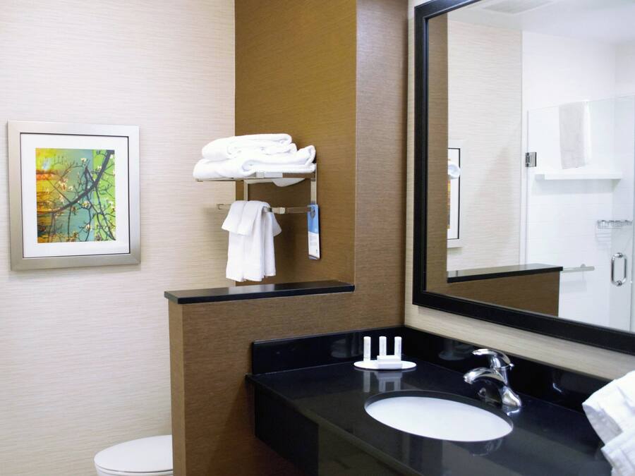 A modern bathroom with a black countertop, a white sink, and a large mirror. There is a framed picture on the wall and a towel rack with folded towels.
