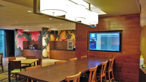 A conference room with a long wooden table, several chairs, a large screen displaying a list, and a kitchen area with wooden cabinets. - Fairfield Inn & Suites Stroudsburg Bartonsville / Poconos (Stroudsburg)