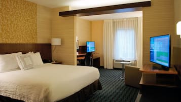 Ein Hotelzimmer mit einem großen Bett, einem Schreibtisch, einem Sessel, einem Fernseher und einem Fenster mit Vorhängen.