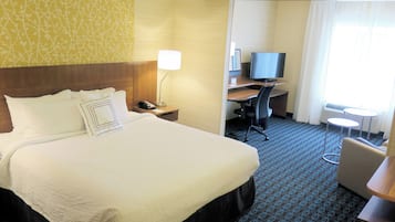 A hotel room with a large bed, a desk with a computer, a TV, and a small table.