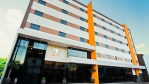 Een modern hotelgebouw met een opvallende oranje verticale strook, grote glasramen en een bord met de tekst 'Megal Suites Hotel'.