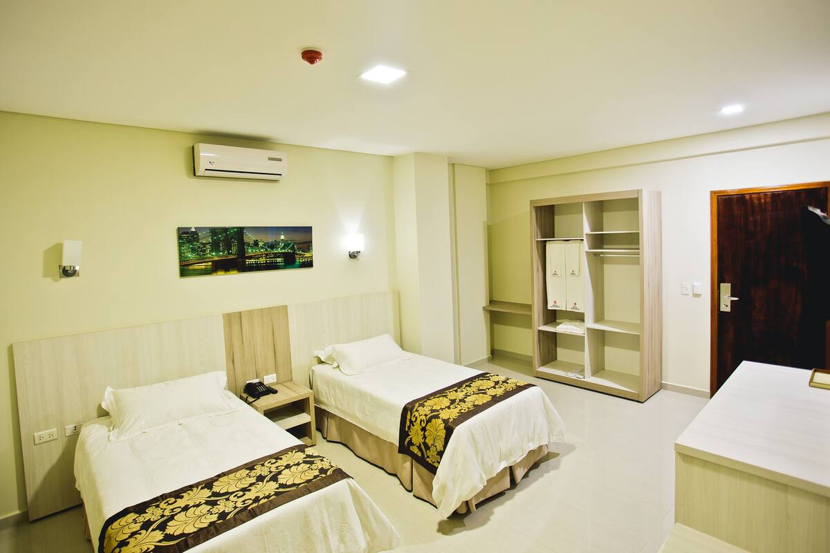 Habitación de hotel con dos camas, un armario, un escritorio y un cuadro en la pared.