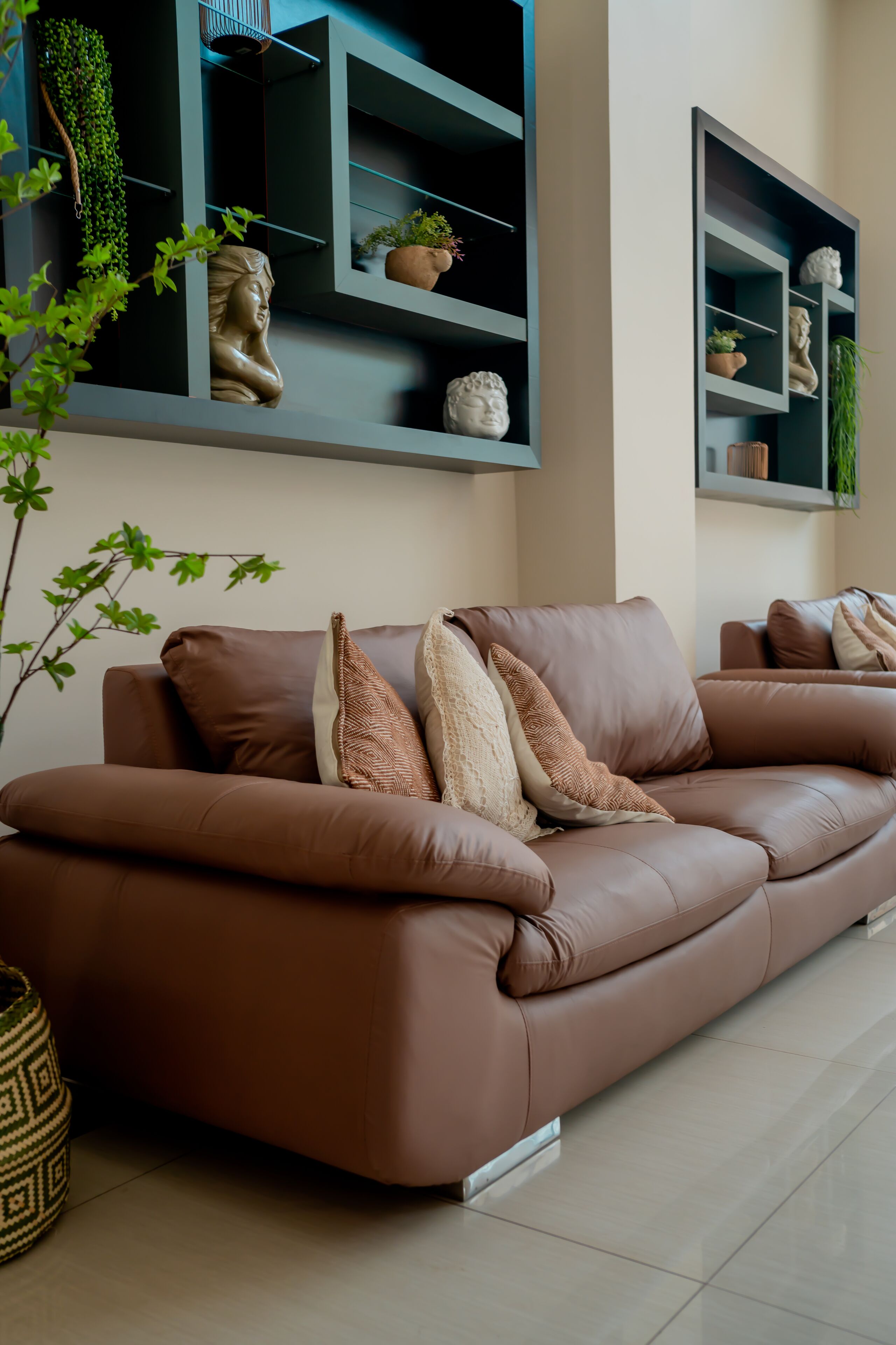 A brown leather sofa with patterned cushions, a potted plant, and a wall-mounted shelf with decorative items.