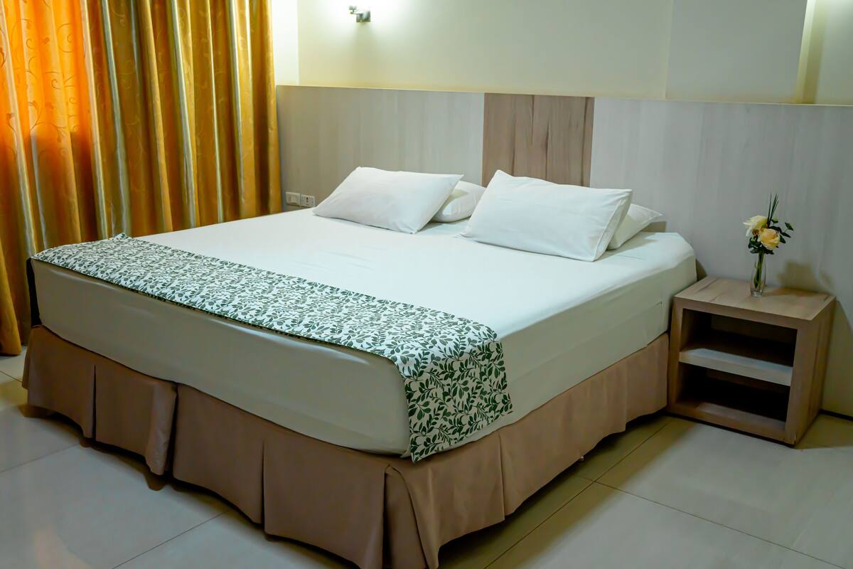 Una cama bien hecha con una colcha estampada y una mesita de noche de madera con un jarrón de flores.