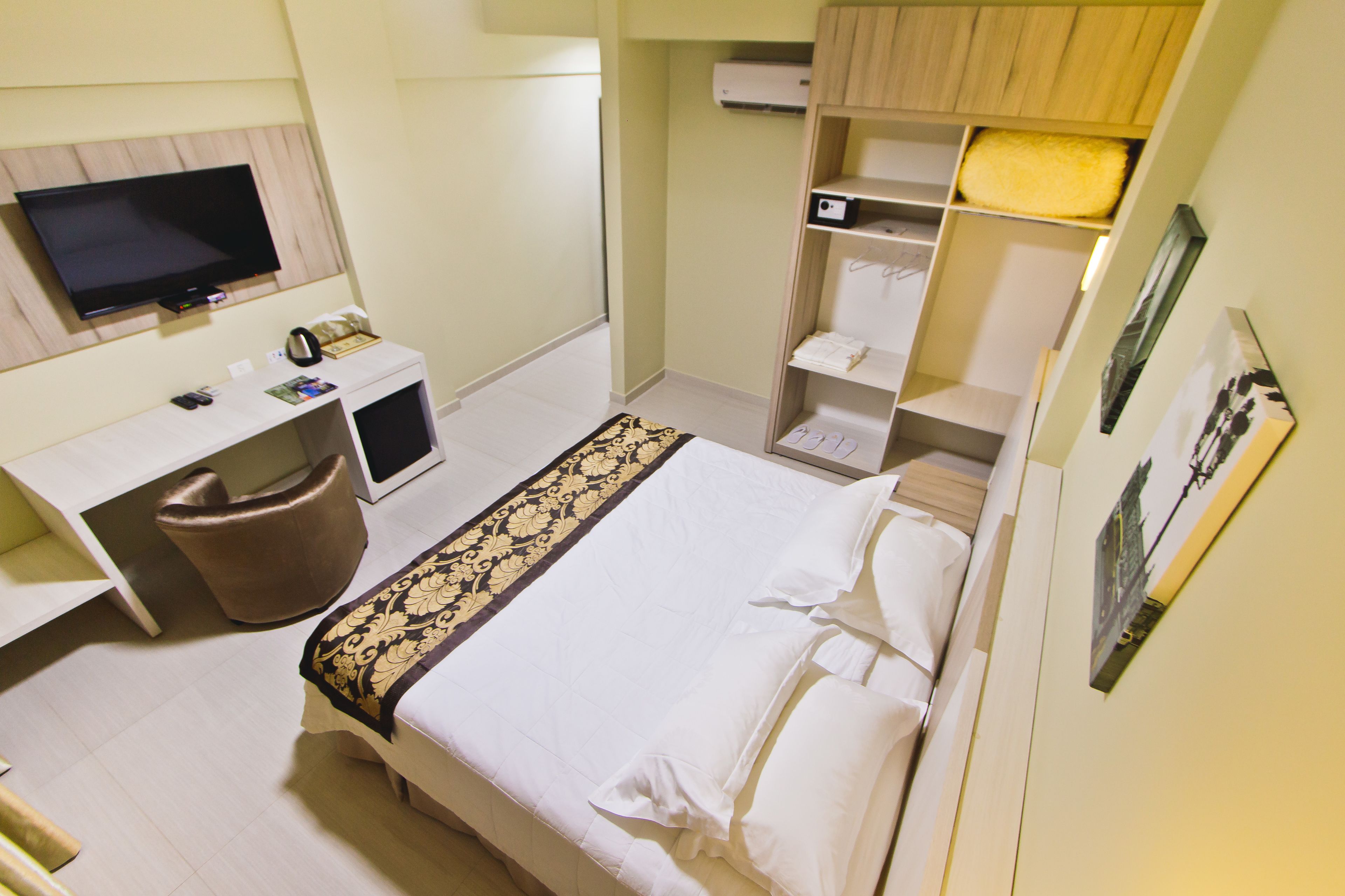 A hotel room with a bed, a desk with a computer, a TV, and a wardrobe.