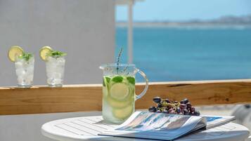 A table with a pitcher of iced drink garnished with mint and lime, a glass of iced drink, and a bunch of grapes on a balcony overlooking the sea.