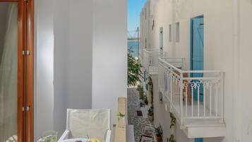 A balcony with a table set for dining, a scooter, and a narrow street with buildings.