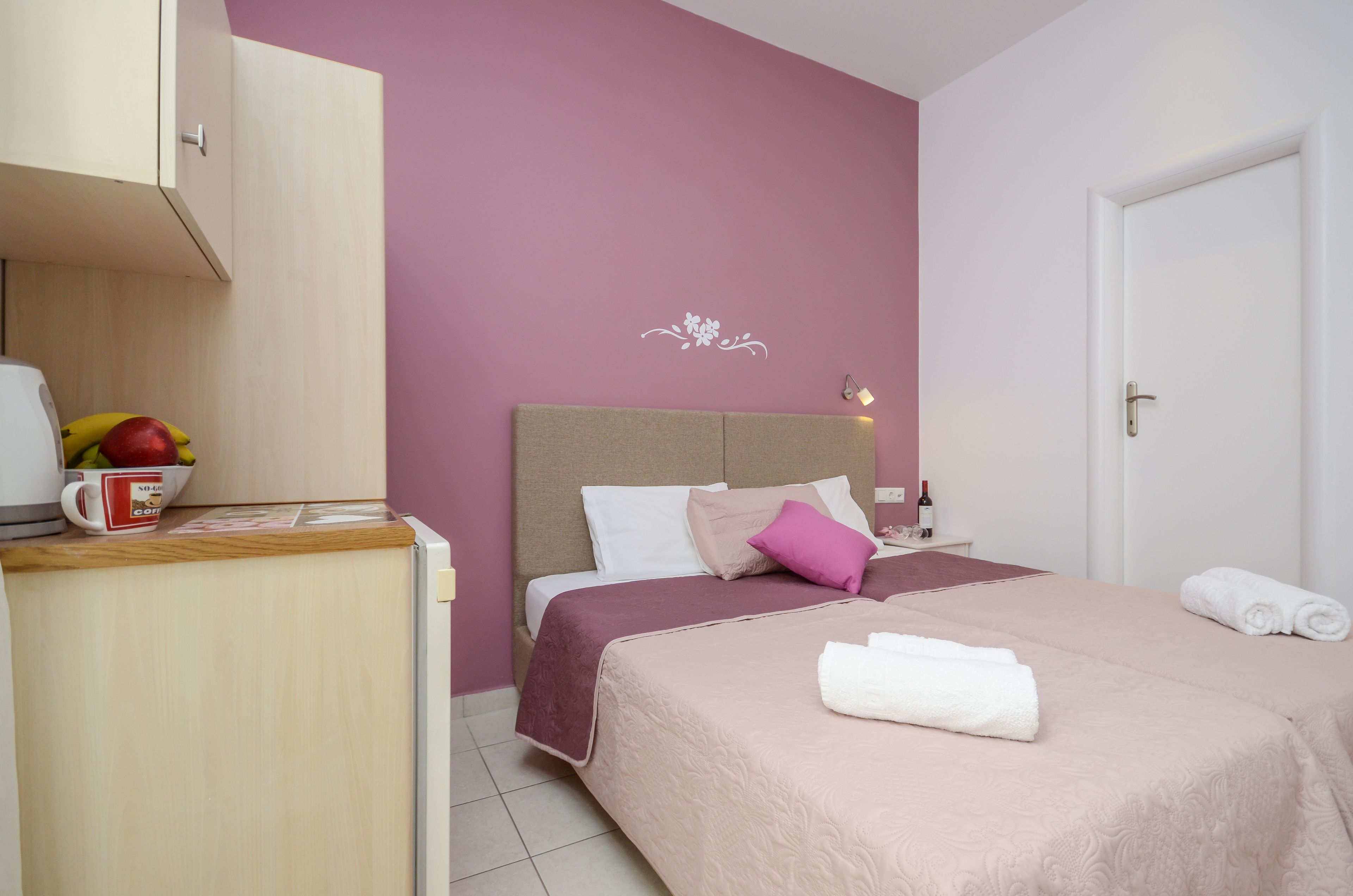 Un dormitorio ordenado con una cama, almohadas, una mesita de noche con una botella y un frutero.