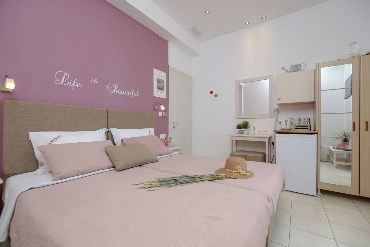A bedroom with a bed, a bedside table, a small desk, a mirror, and a wardrobe.