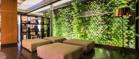 A modern hotel lobby with a green vertical garden wall, cushioned seating, and a large window.