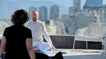 Two people meditating on yoga mats with a cityscape in the background.