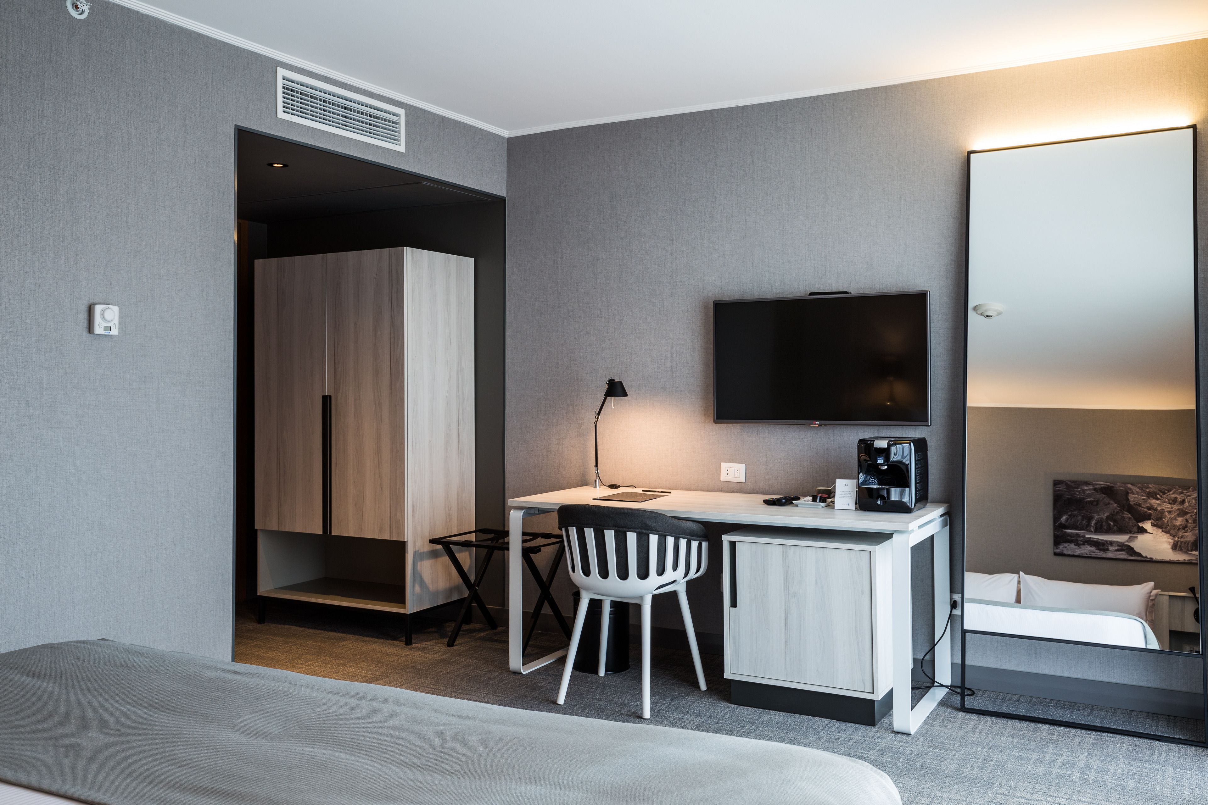Una moderna camera d'albergo con un letto, una scrivania con una sedia, una TV a schermo piatto, una macchina per il caffè e un armadio.