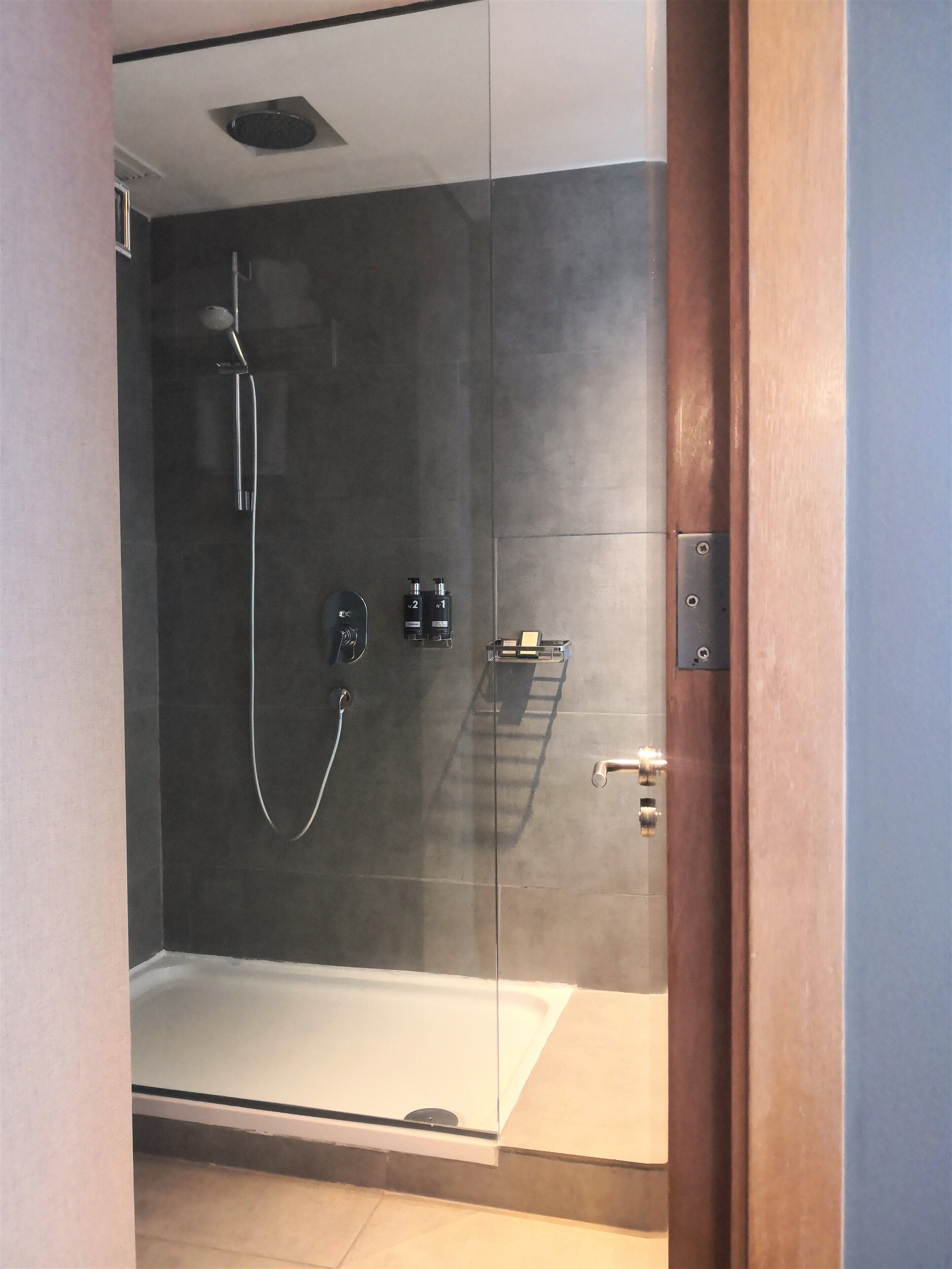A modern shower with a glass door, a handheld showerhead, and a control panel with two bottles.
