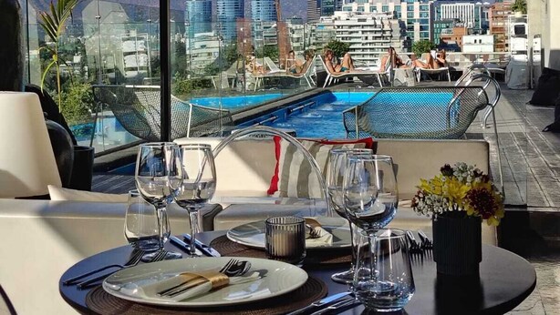 Un área de comedor en la azotea con vistas a un paisaje urbano y montañas.