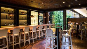 Una zona de bar con sillas blancas, una barra larga y estantes con botellas.