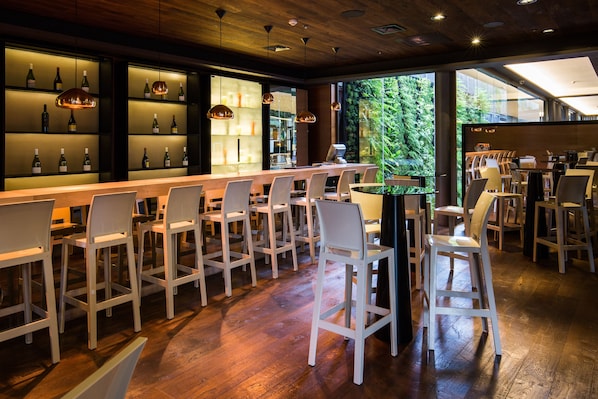 A bar area with white chairs, a long counter, and shelves with bottles. - Solace Hotel Santiago (Santiago)