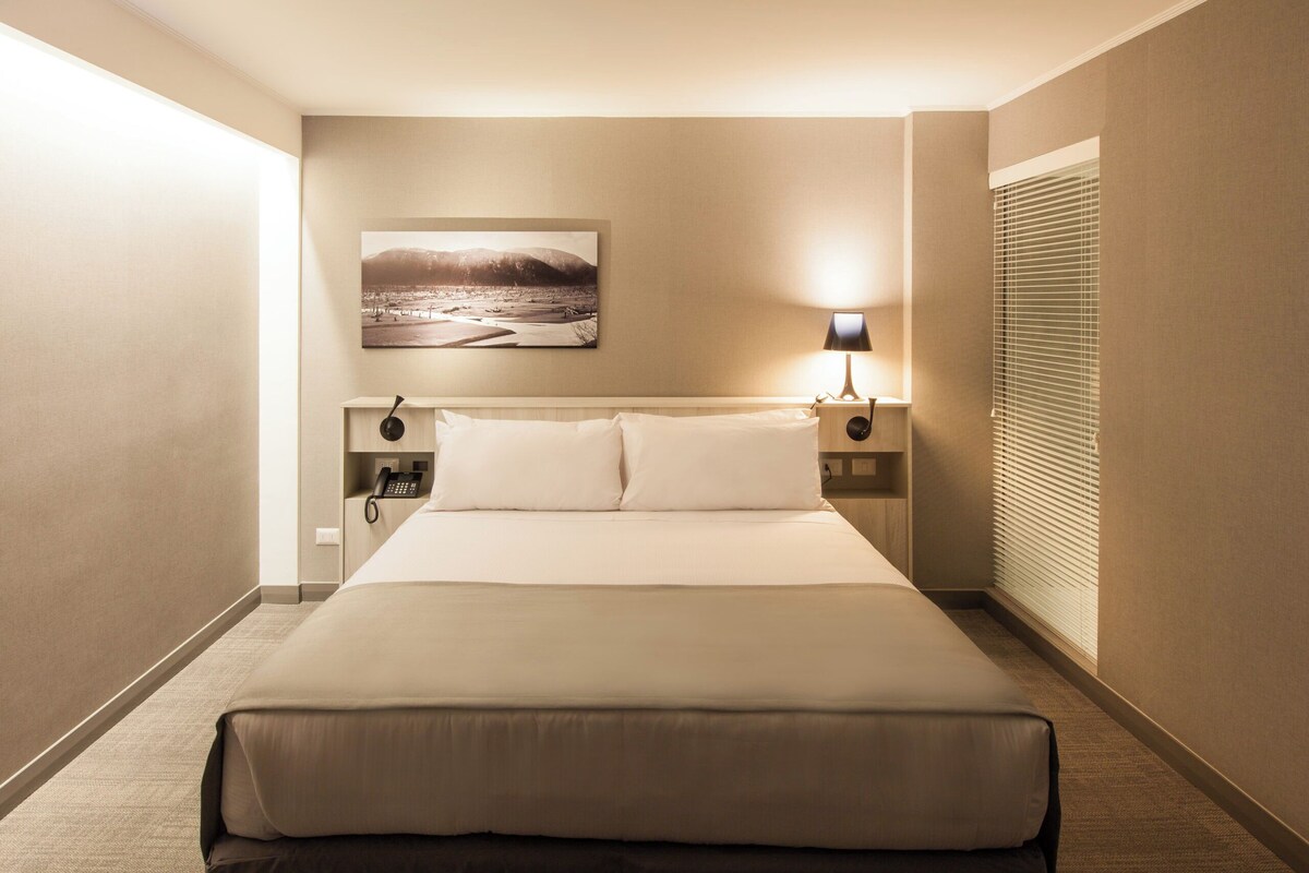 Une chambre d’hôtel avec un grand lit, une lampe de chevet, un téléphone et un tableau au mur.