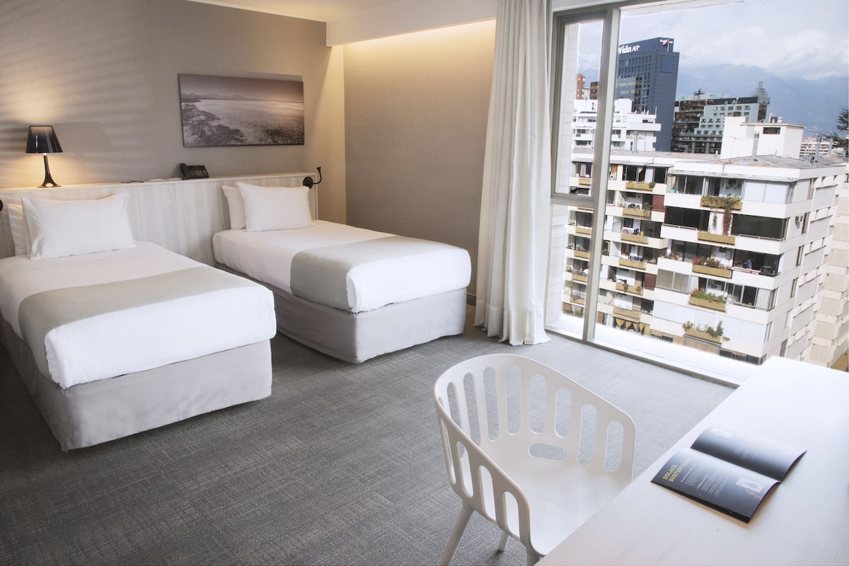 Une chambre d’hôtel avec deux lits, un bureau et une vue sur la ville.