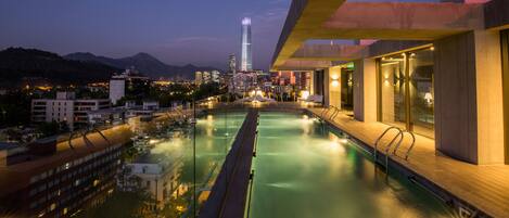 Una piscina en la azotea con vistas a un horizonte urbano y montañas al fondo.