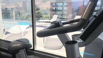 A gym with exercise equipment, a pool, and a view of buildings and hills.