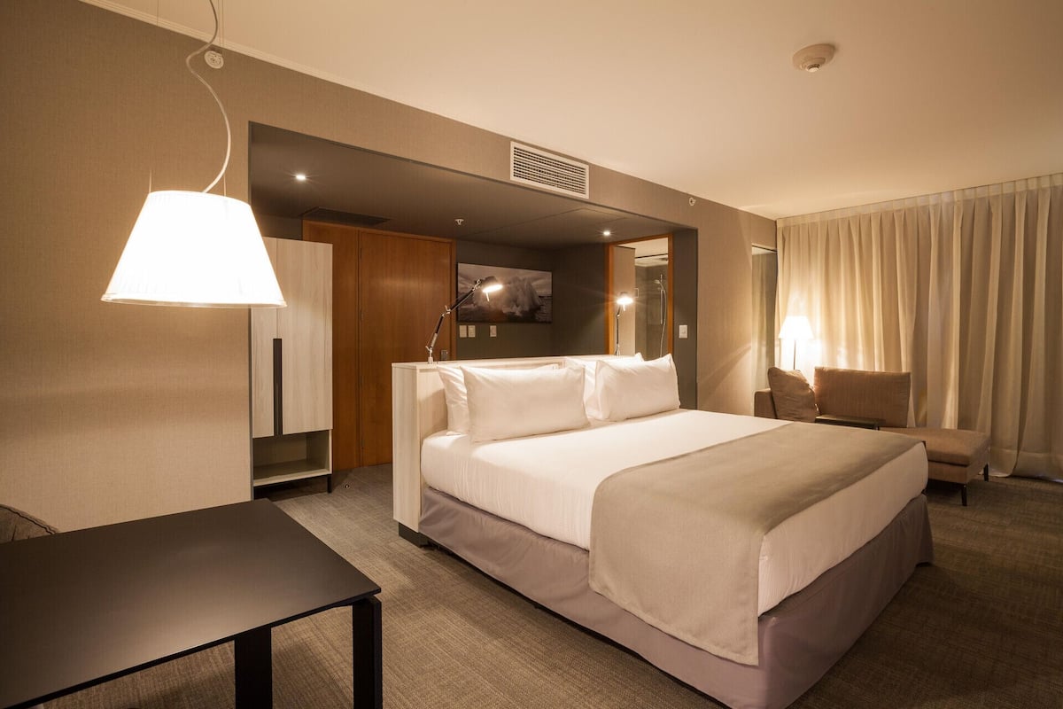 Une chambre d’hôtel avec un lit, une table de chevet, une lampe et une vue sur l’extérieur par une fenêtre.