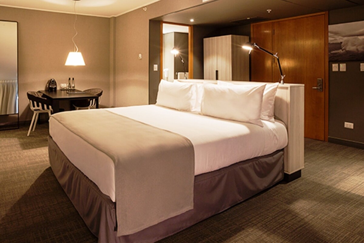 Une chambre d’hôtel comprenant un lit, un bureau, une chaise, une lampe, une armoire et un tableau au mur.