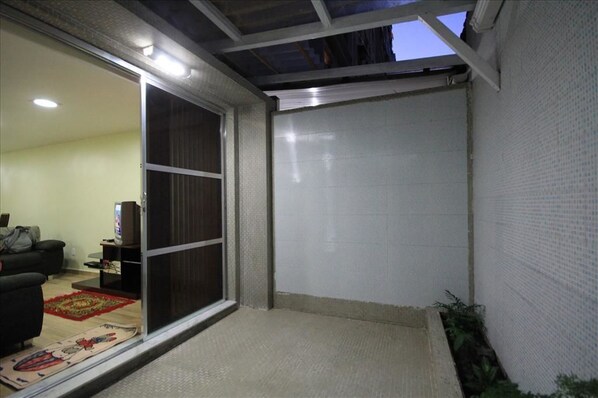 A room with a sliding glass door leading to a balcony, a small seating area with a sofa and a TV, and a tiled wall.